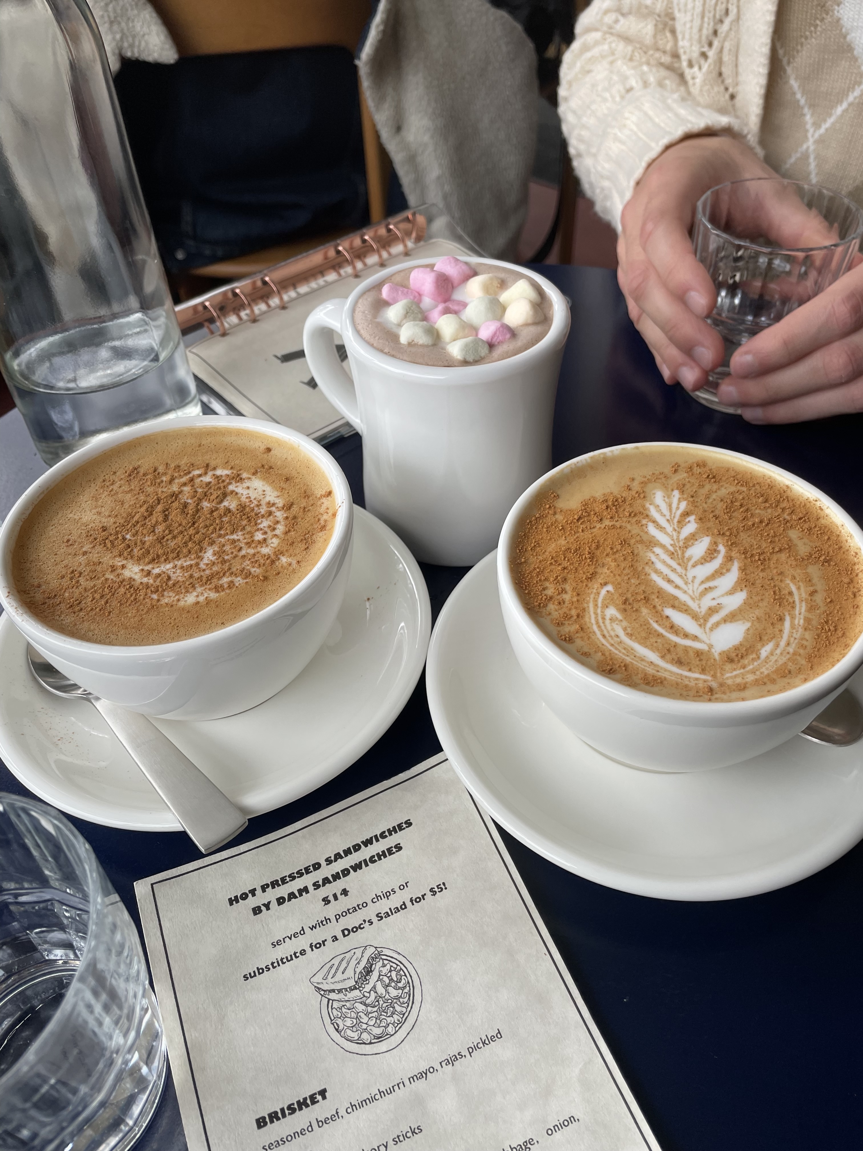 Three mugs of coffee and hot chocolate on a café table with friends.