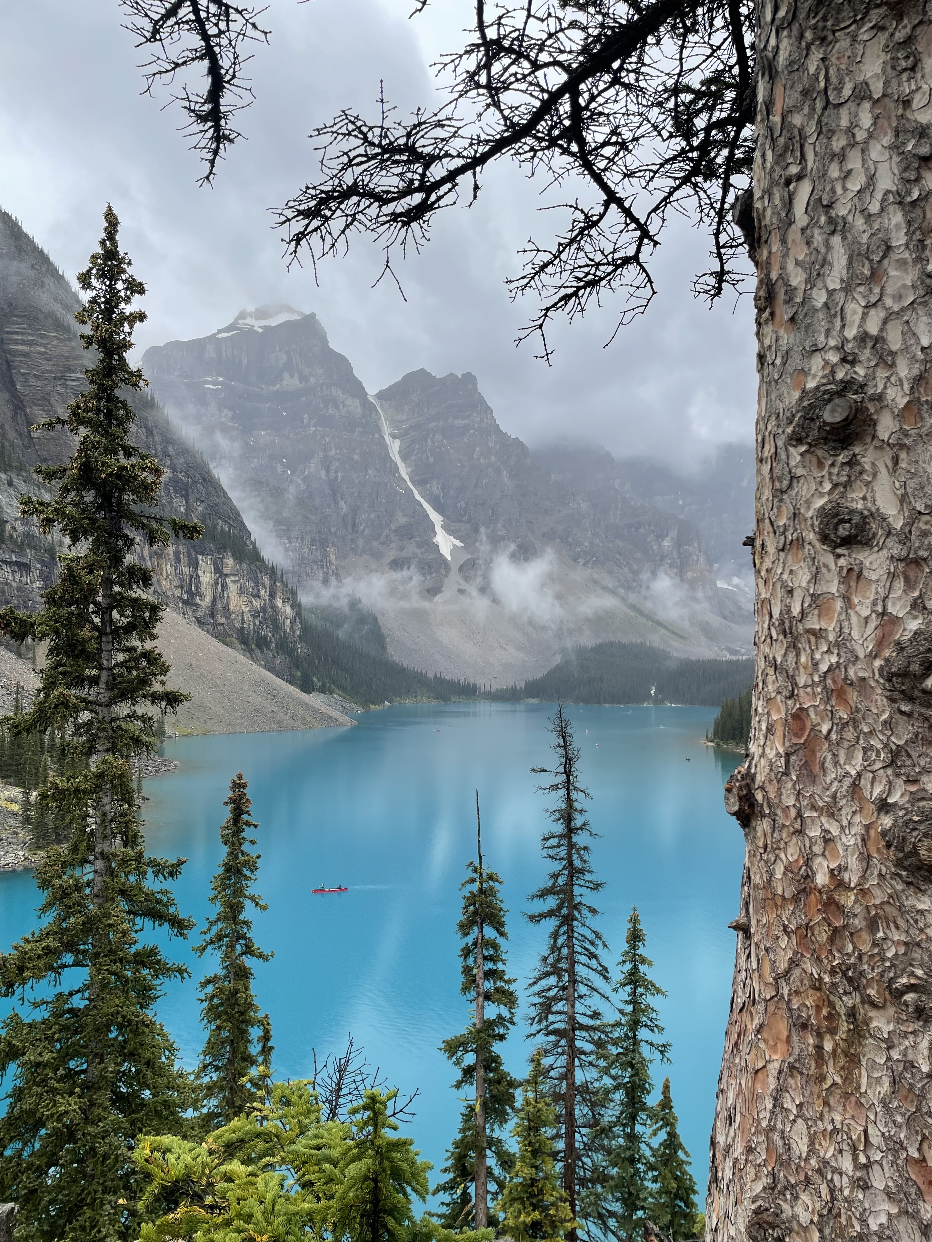 Turquoise mountain lake surrounded by evergreen trees and misty peaks.